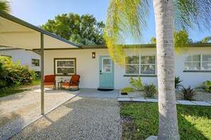A house with a covered patio, two rocking chairs, a door, and a small garden with plants and a palm tree. - Paradise Del Sol by Gulf Beaches: Endless Summer! (Nokomis)
