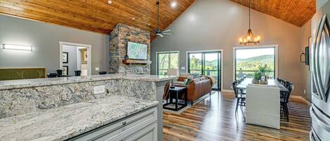 A spacious kitchen with granite countertops, a stone fireplace, and a dining area with a high ceiling and wooden beams.