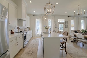 A spacious kitchen with a central island, white cabinetry, and a modern chandelier.