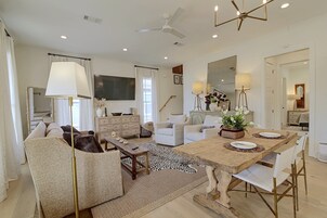 A spacious living room with a sofa, a dining table set for four, and a large flat-screen TV mounted on the wall.