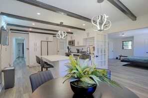A modern kitchen with white cabinets, a dining area with a table and chairs, and a living room with a bed and a window.