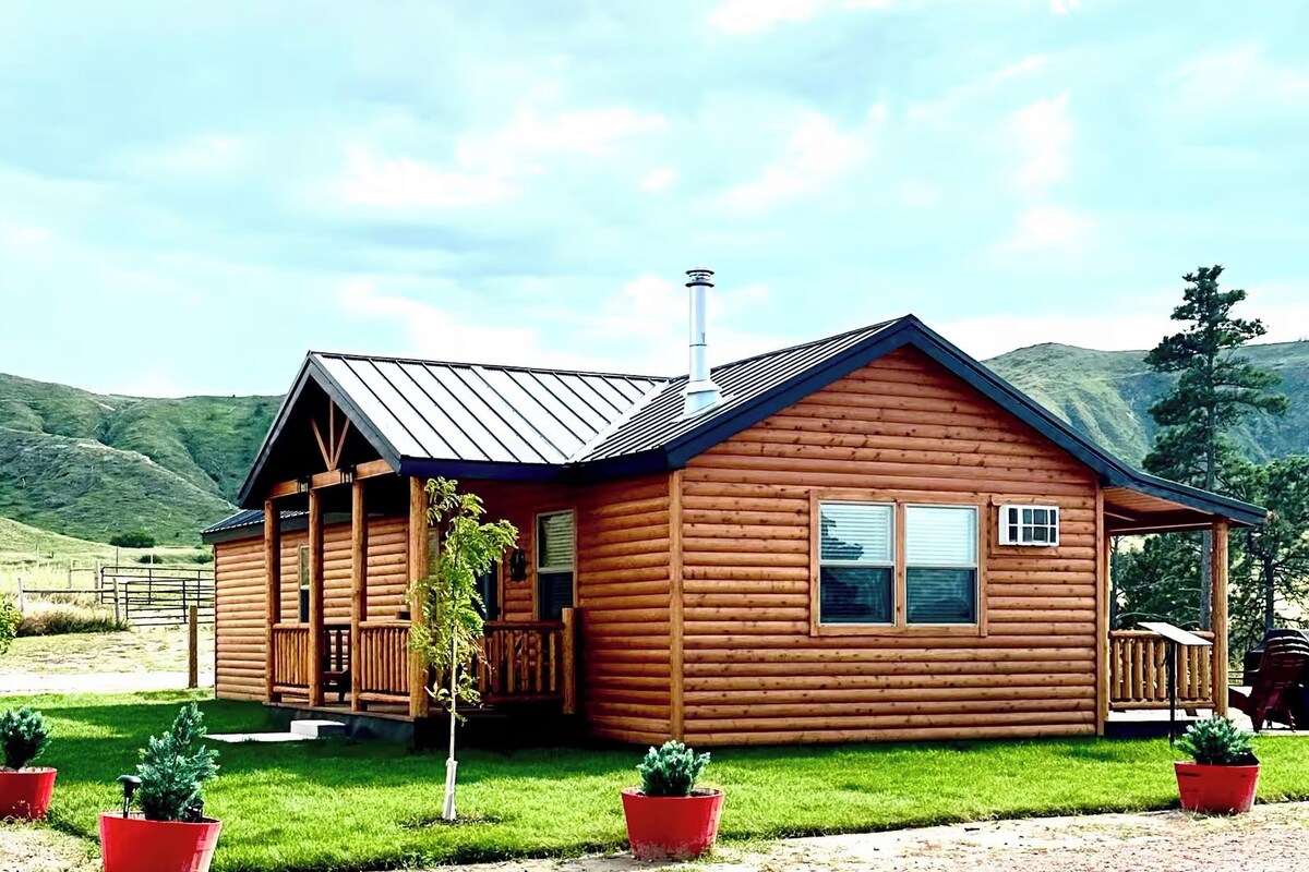 A wooden cabin with a porch, a chimney, and a fenced yard.