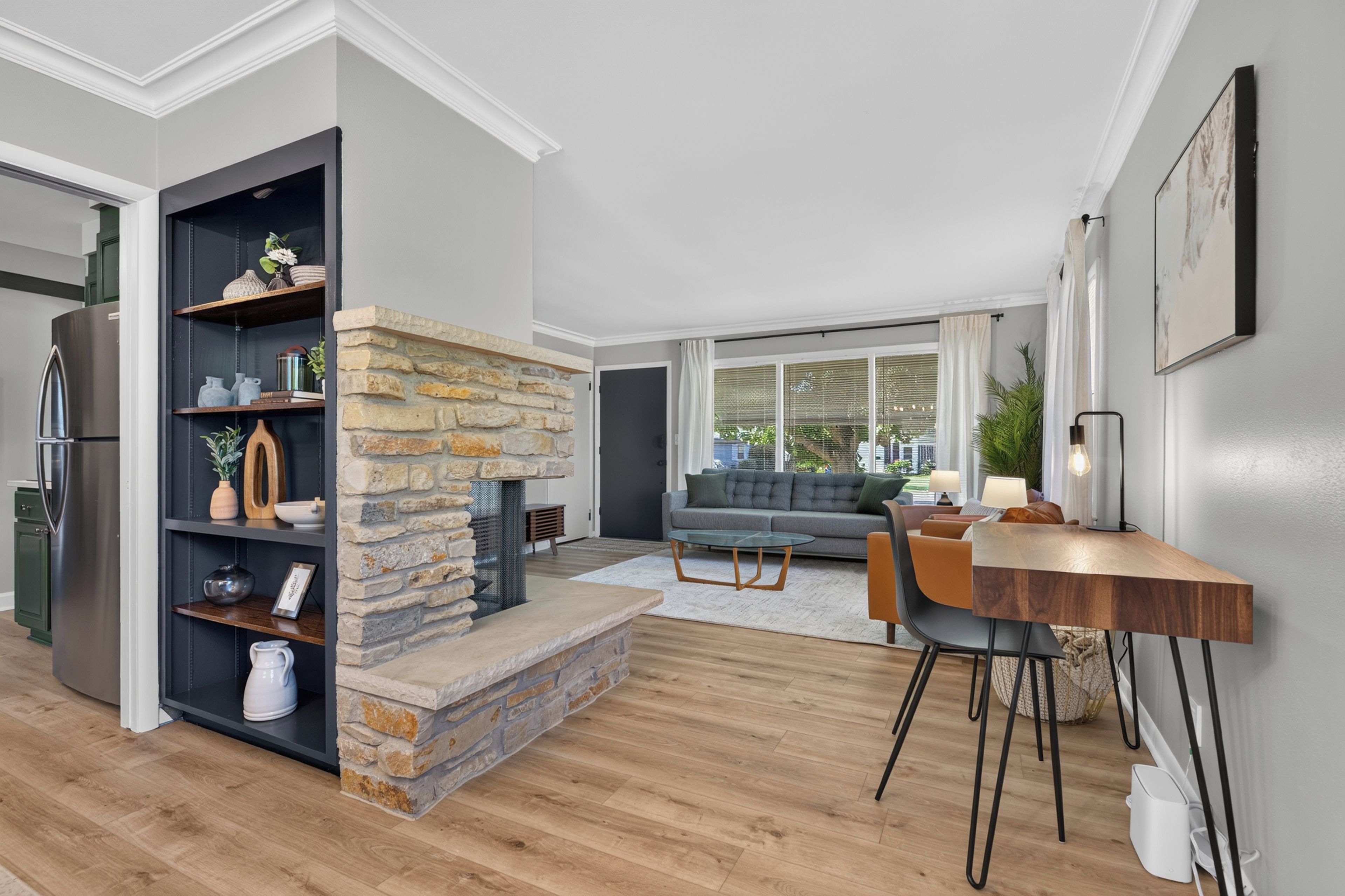 A modern living room with a stone fireplace, a dining area with a wooden table, and a kitchen with a built-in refrigerator.