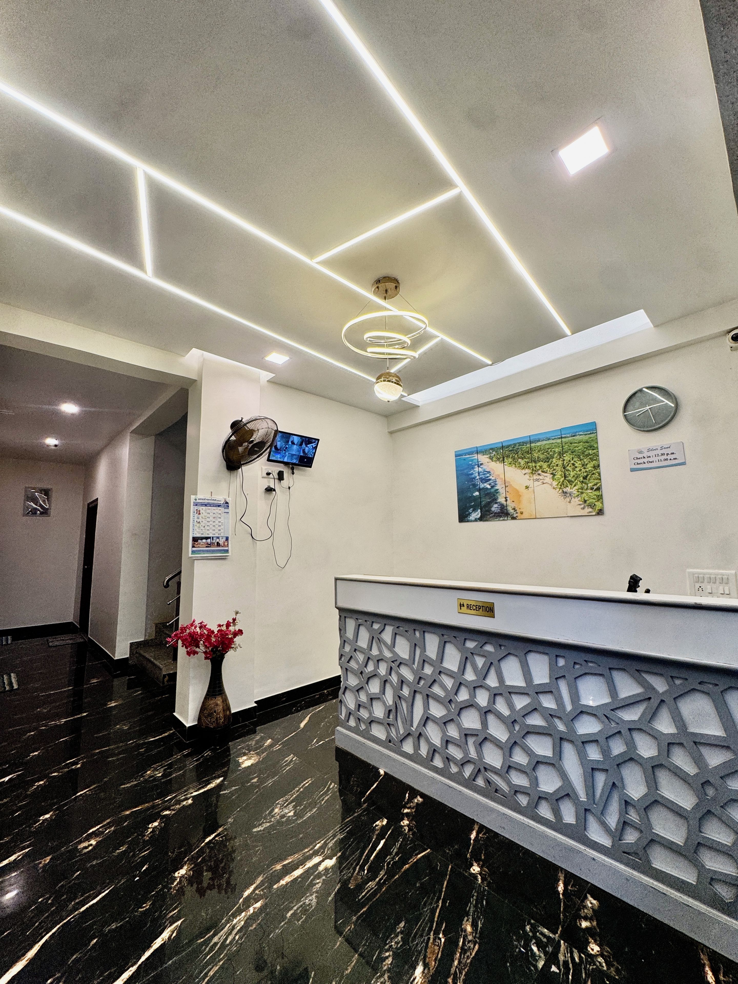 A reception area with a marble floor, a reception desk, a wall-mounted clock, a television, and a framed picture.
