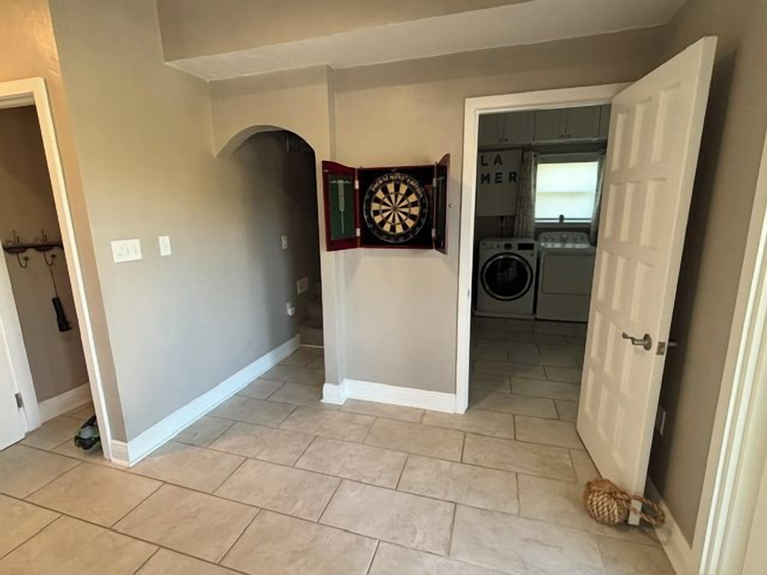 A hallway with a dartboard, a laundry room in the background, and a cat on the floor.