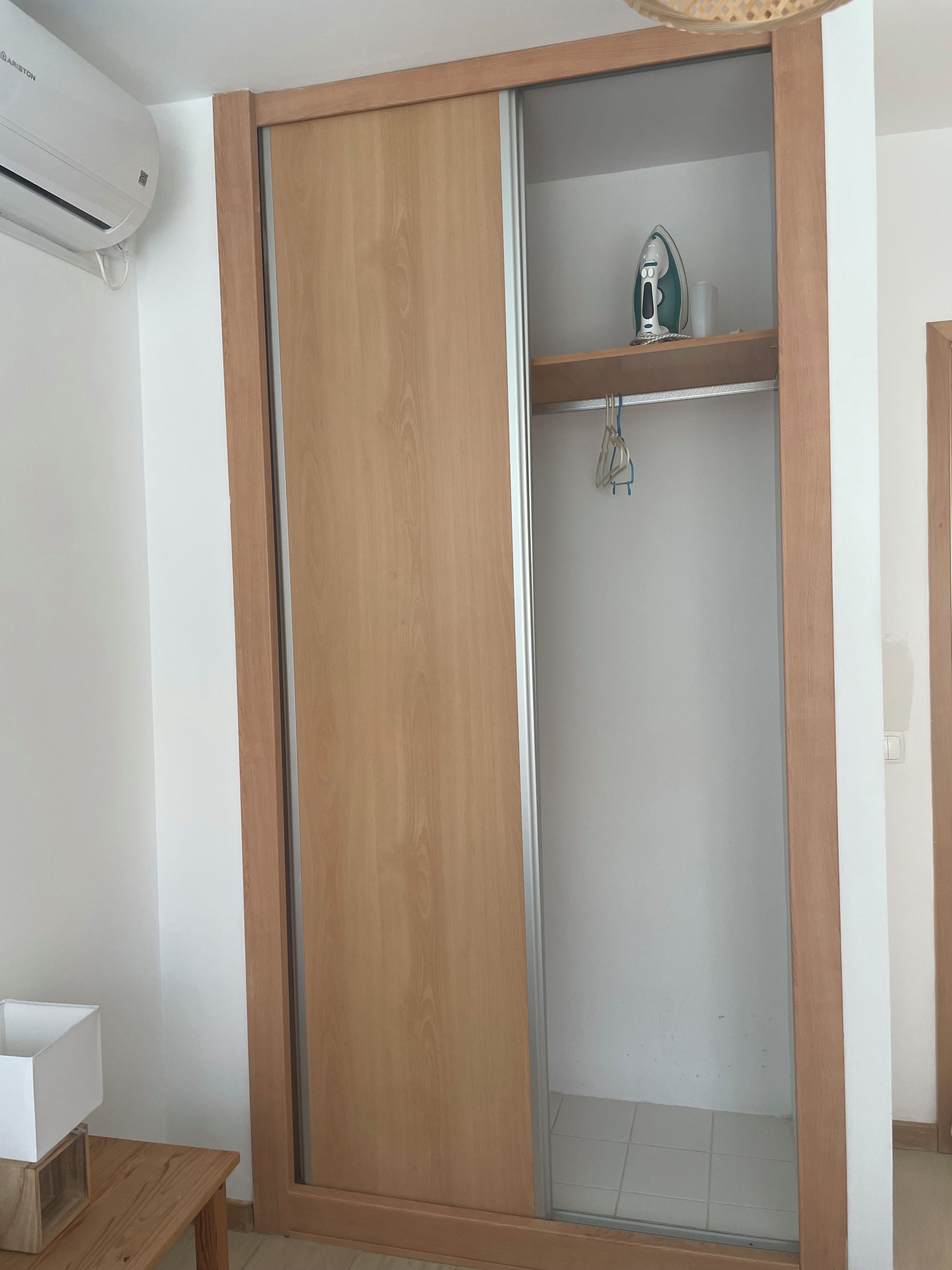 Una habitación con un armario de madera, un aire acondicionado blanco y un pequeño estante con una tetera y un gancho.
