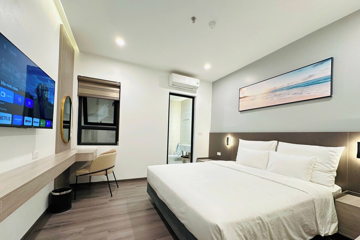 Habitación de hotel con cama, un escritorio con silla, un televisor en la pared y una ventana.