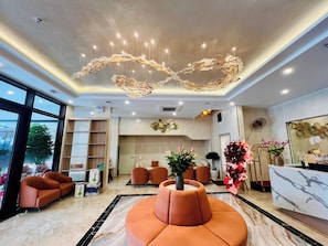 Vestíbulo de hotel con mostrador de recepción, zona de estar y una lámpara decorativa en el techo.