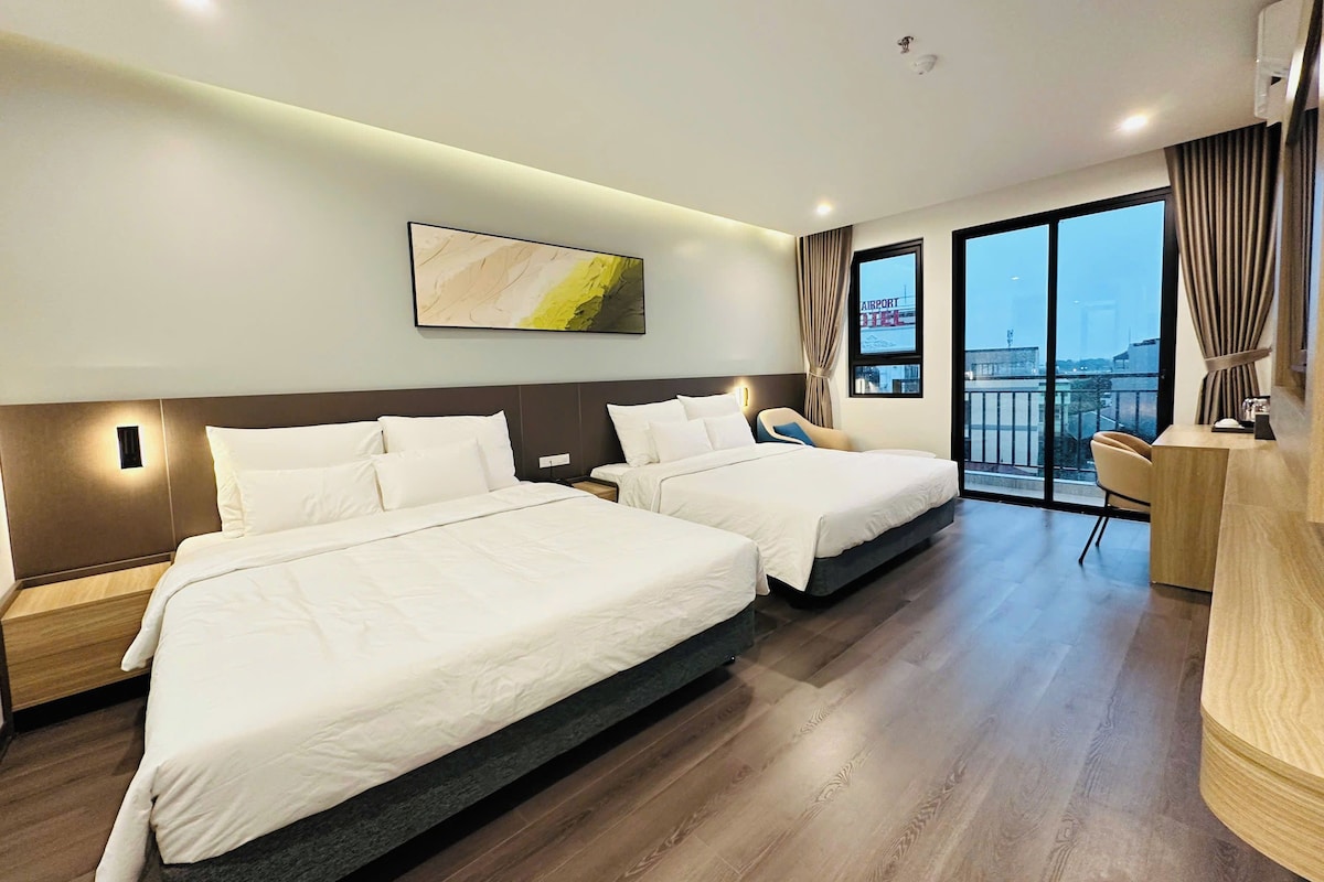 Habitación de hotel con dos camas, un escritorio, una silla y un ventanal con vistas a la ciudad.