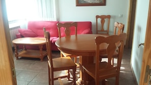 A dining area with a wooden table and chairs, a pink sofa, and a window with curtains.