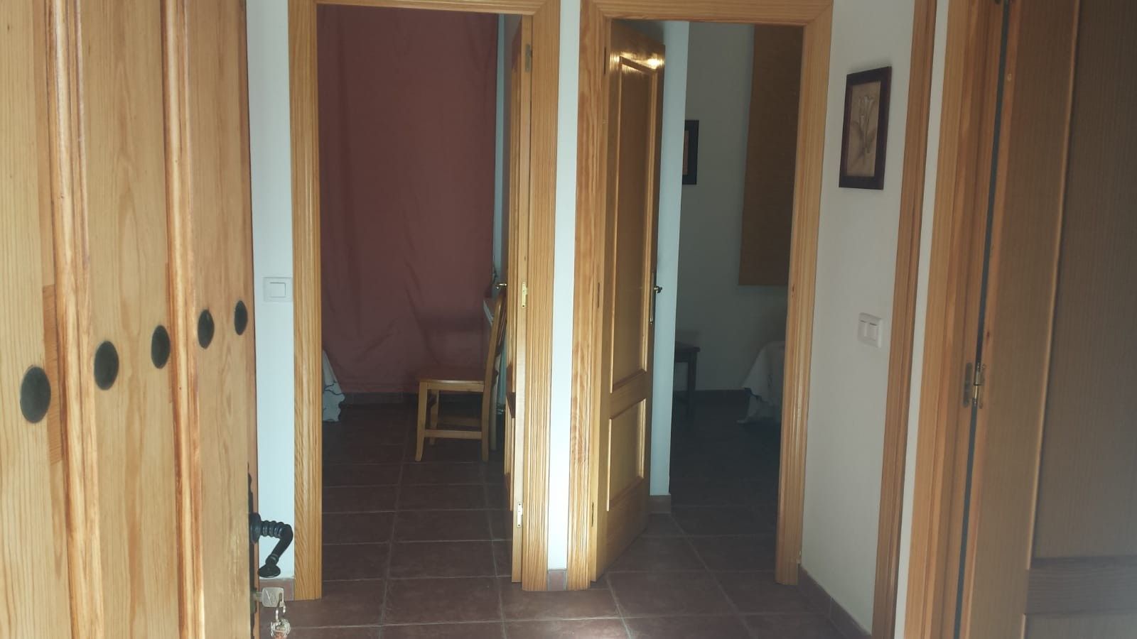 A hallway with wooden doors, a chair, and a bed in the background.