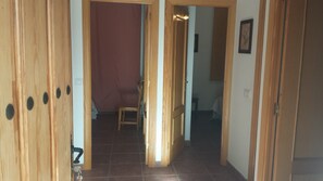 A hallway with wooden doors, a chair, and a bed in the background.