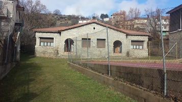 Un edificio in pietra con tetto in tegole rosse, un cortile recintato e uno sfondo collinare.