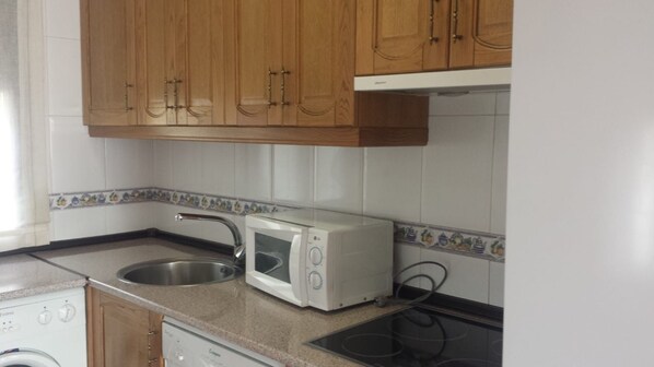 A kitchen with wooden cabinets, a microwave, a sink, and a stove.