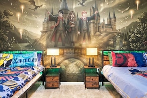 Un dormitorio con dos camas, cada una con una colcha temática, un mural de un castillo y un puente de piedra.