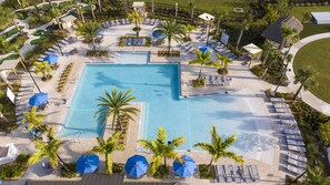Ein großer rechteckiger Pool mit Liegestühlen und Sonnenschirmen, umgeben von Palmen und einem gepflegten Rasen.
