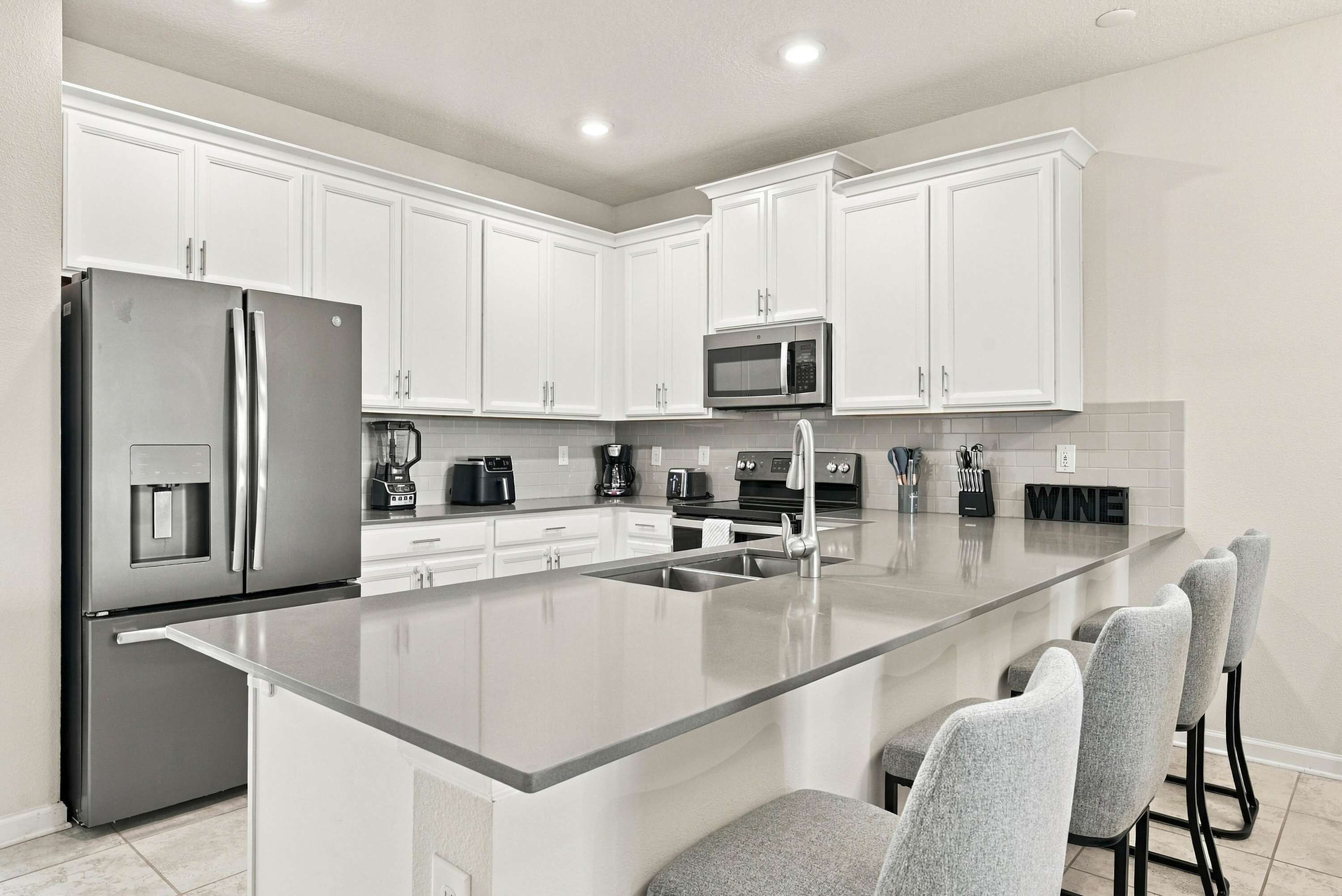 Una cocina moderna con armarios blancos, electrodomésticos de acero inoxidable y una isla central con taburetes de bar.