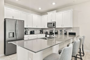 Una cocina moderna con armarios blancos, electrodomésticos de acero inoxidable y una isla central con taburetes de bar.