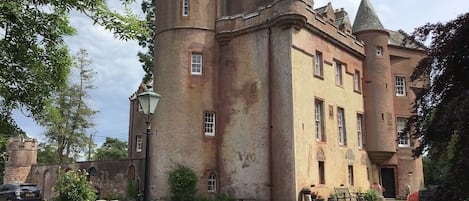 Un bâtiment historique doté d’une tour centrale, d’une cour avec un chemin de gravier et d’une pelouse.