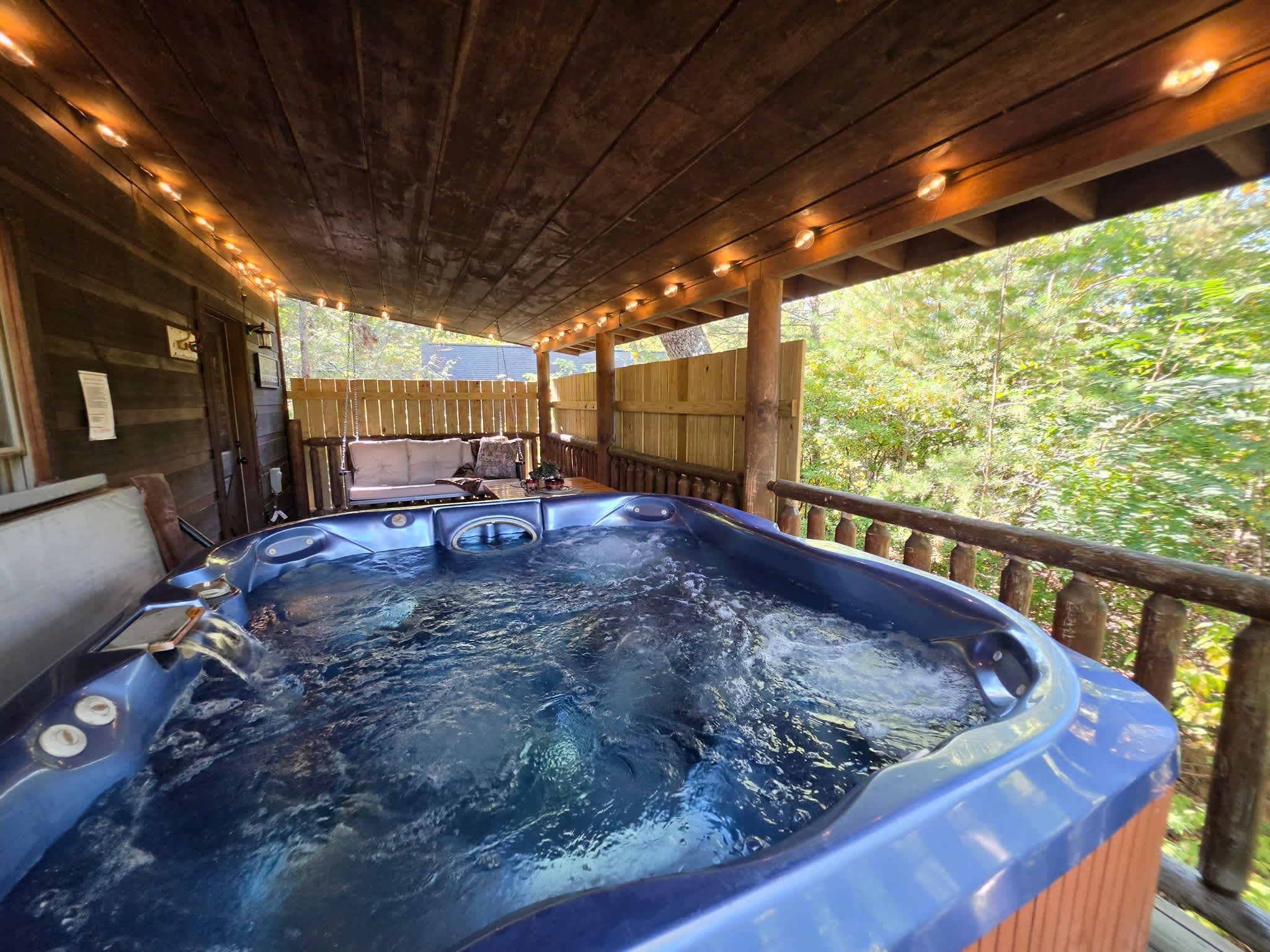 Un bain à remous installé sous une terrasse en bois, avec vue sur les arbres.