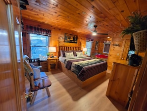 A wooden cabin bedroom with a bed, a chair, a desk, and a red hot tub. - Hot Tub-fireplace-pool Table-arcade-private-relax (Sevierville)