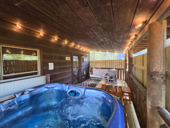 A wooden cabin interior with a hot tub, a wooden deck, and string lights. - Hot Tub-fireplace-pool Table-arcade-private-relax (Sevierville)