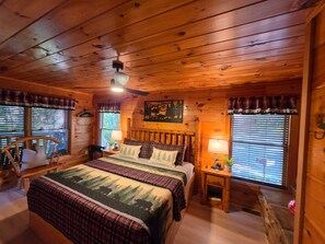 A cozy cabin bedroom with a wooden ceiling, a bed with plaid bedding, two bedside tables with lamps, and a window with blinds. - Hot Tub-fireplace-pool Table-arcade-private-relax (Sevierville)