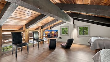 A room with a sloped ceiling, wooden beams, a television, and seating.