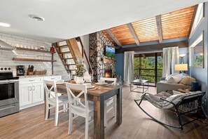 Una cocina moderna con armarios blancos, un comedor con mesa de madera y una chimenea de piedra.