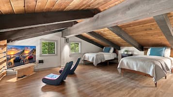 A cozy attic bedroom with a sloped ceiling, wooden beams, a bed, two bedside tables, a chair, and a large window.