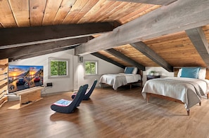 A cozy attic bedroom with a sloped ceiling, wooden beams, a bed, two bedside tables, a chair, and a large window. - 2BR Top-floor Condo With Views Resort Amenities (Sevierville)