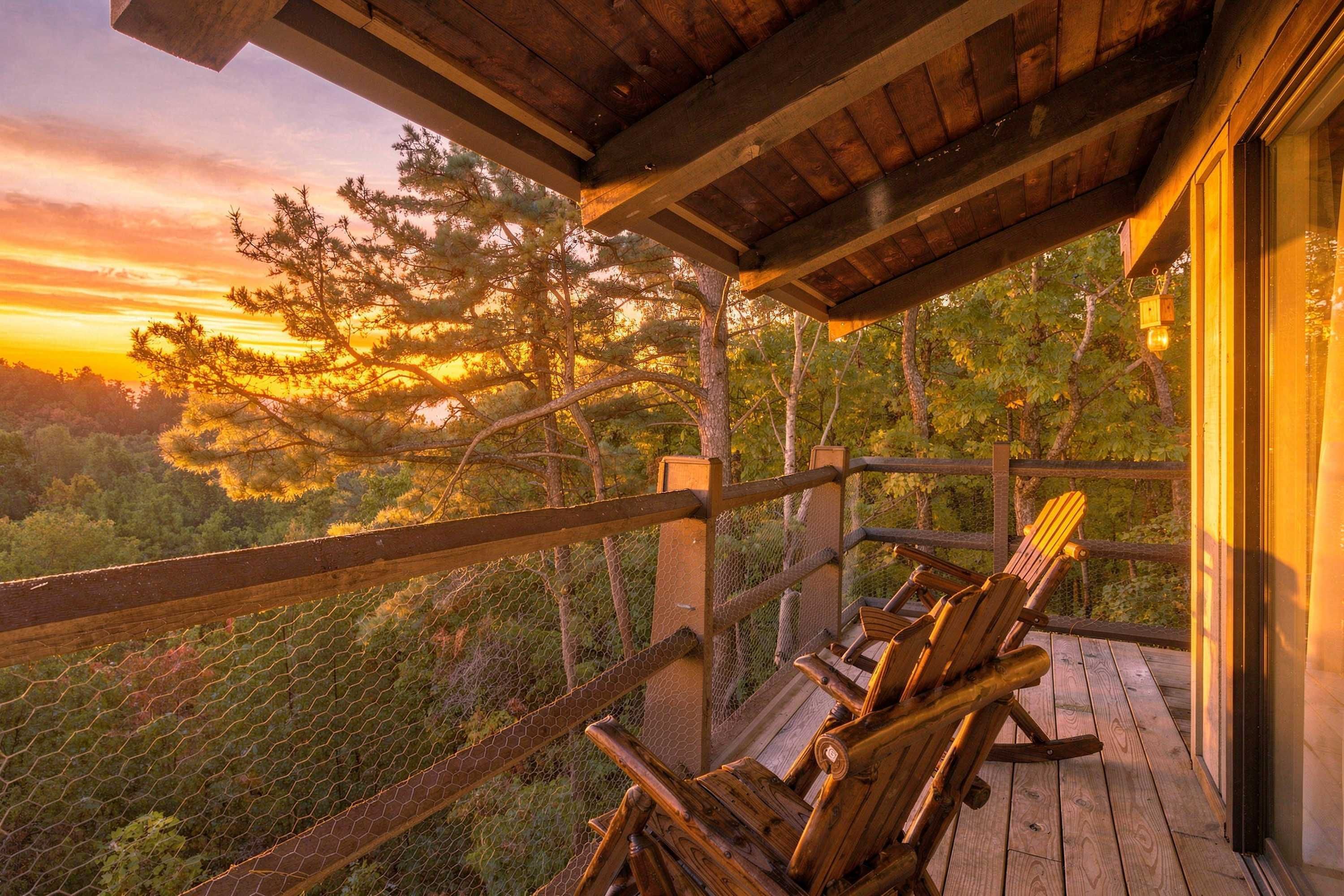 A wooden deck with a view of a forest and a sunset.