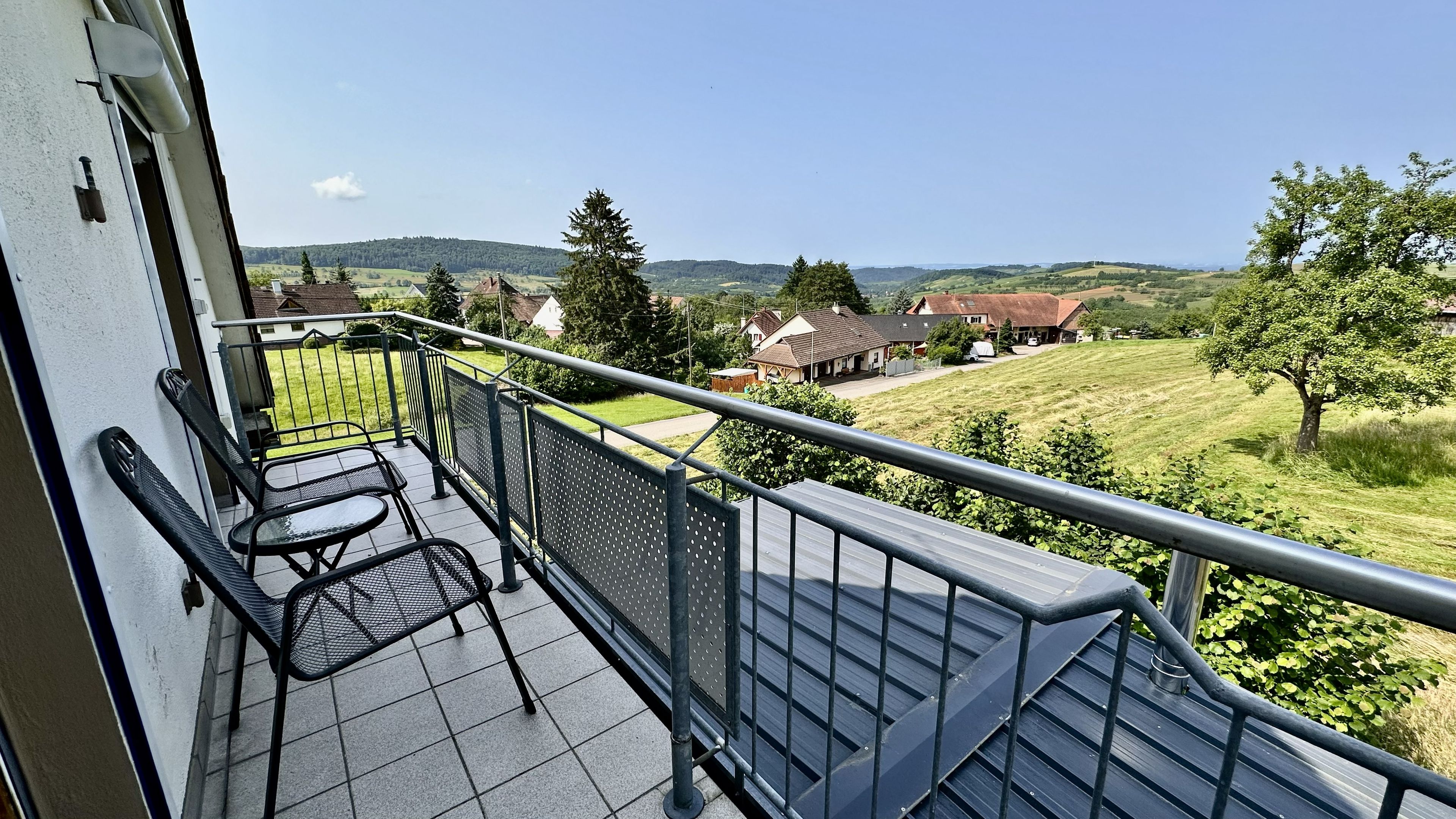 A balcony with a metal railing, two chairs, and a table.