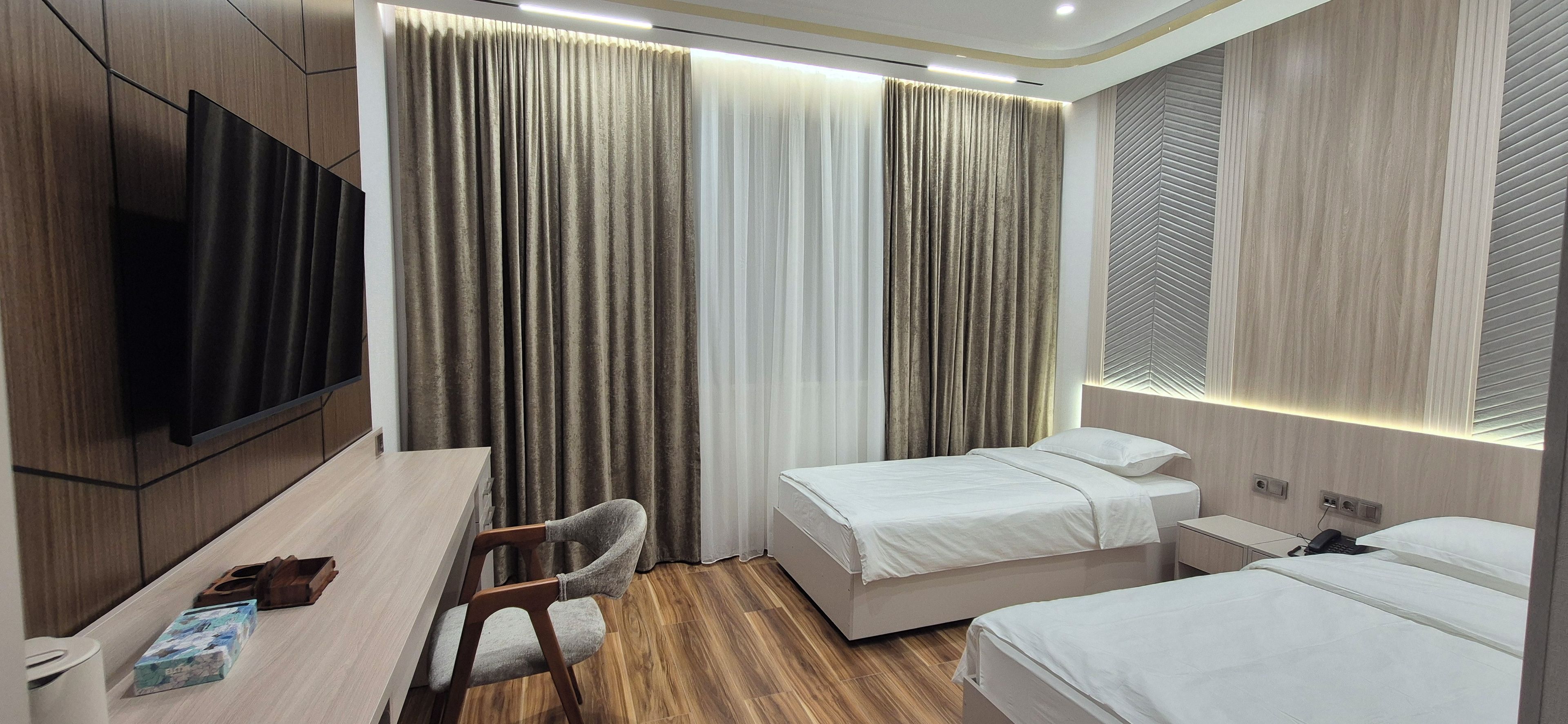 Una habitación de hotel con una cama, mesitas de noche, un escritorio, una silla, un televisor y cortinas.