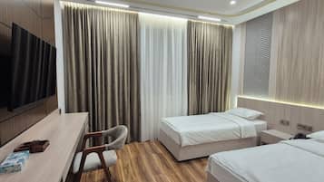 Una habitación de hotel con una cama, mesitas de noche, un escritorio, una silla, un televisor y cortinas.