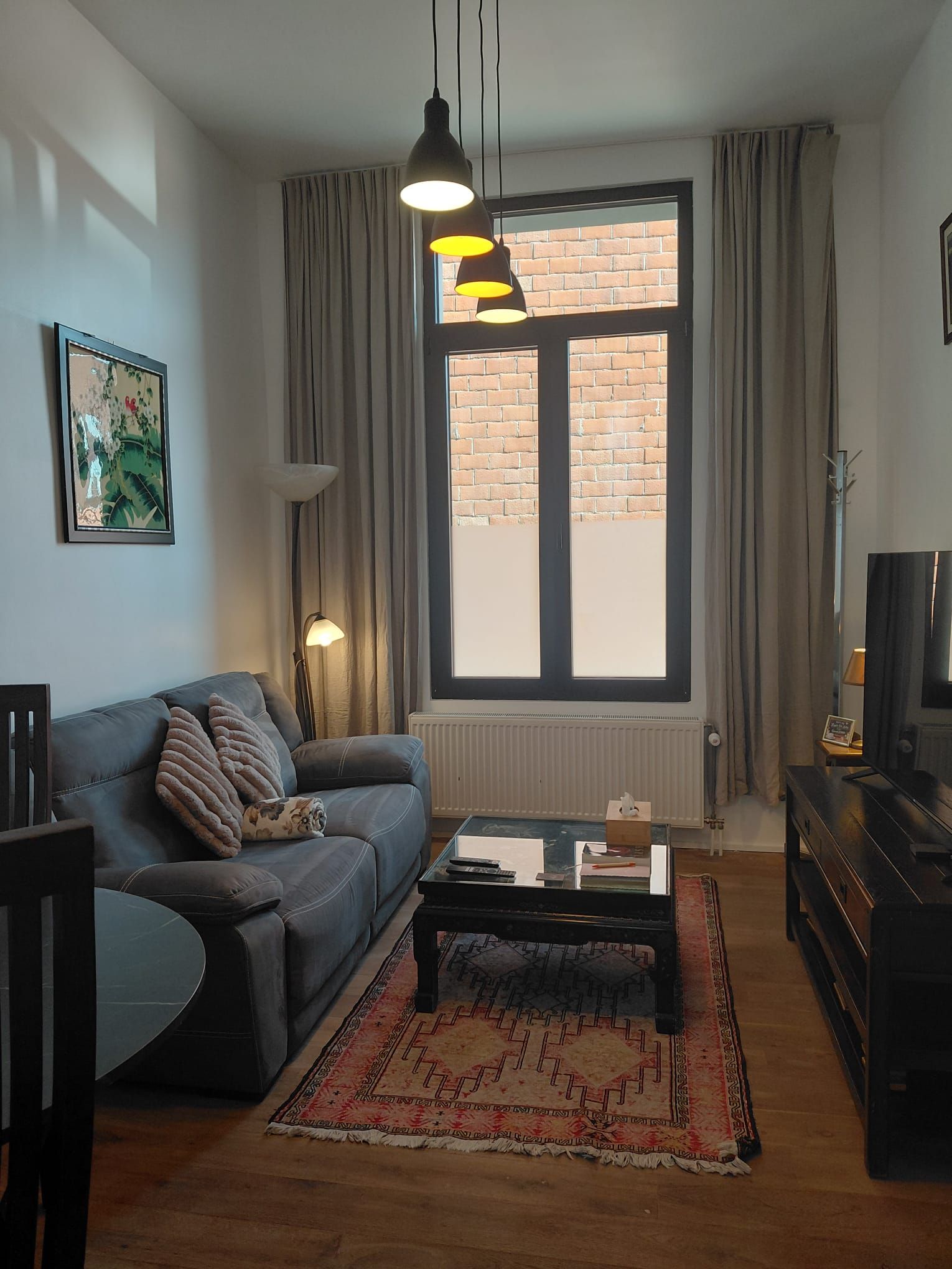 A living room with a sofa, coffee table, and a large window with curtains.