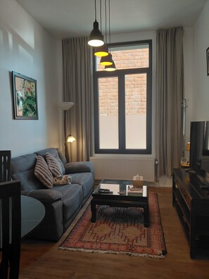 A living room with a sofa, coffee table, and a large window with curtains. - New Listing (Antwerpen)