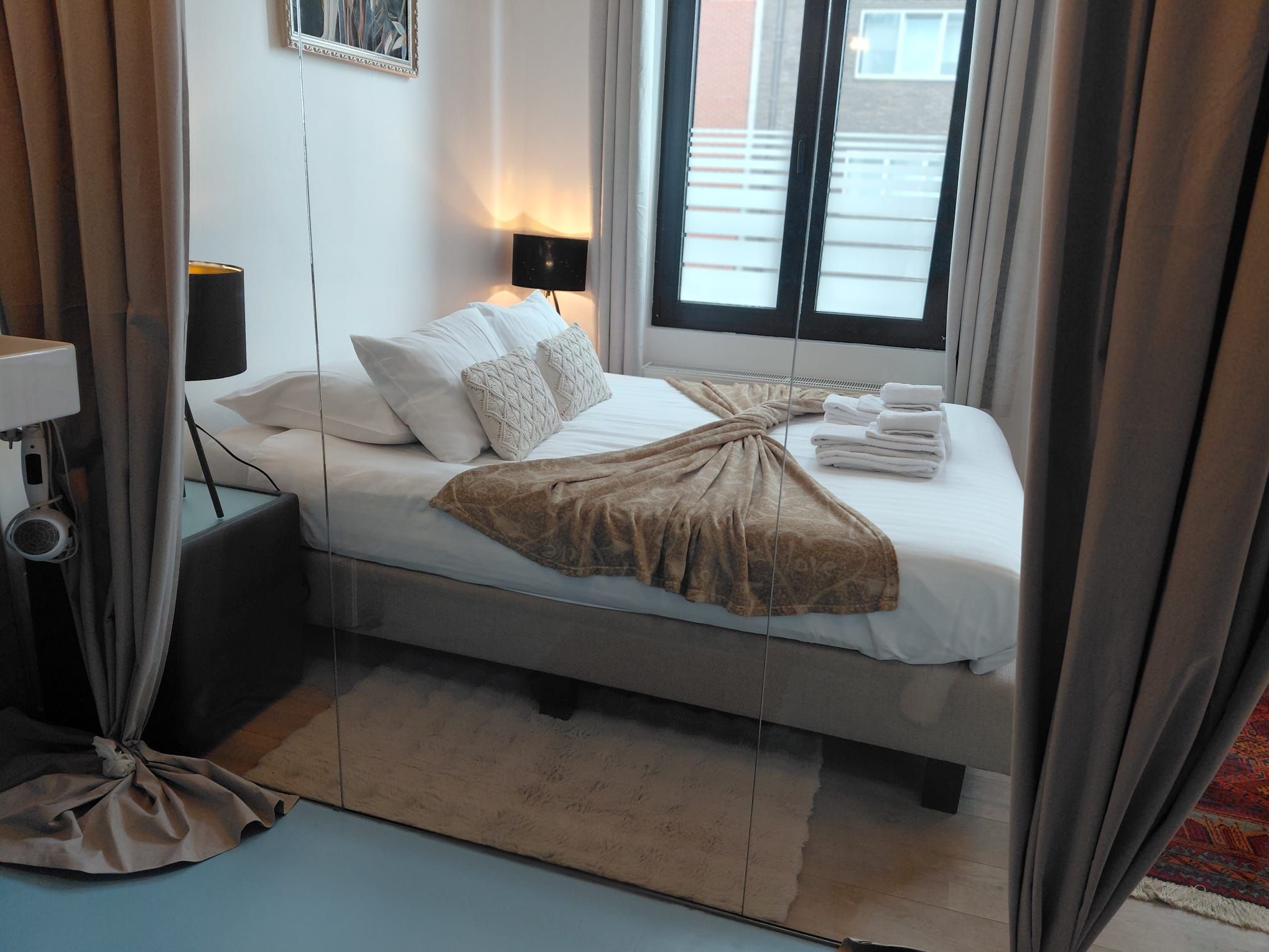 A hotel room with a bed, a bedside lamp, a window, and a view of the outside.
