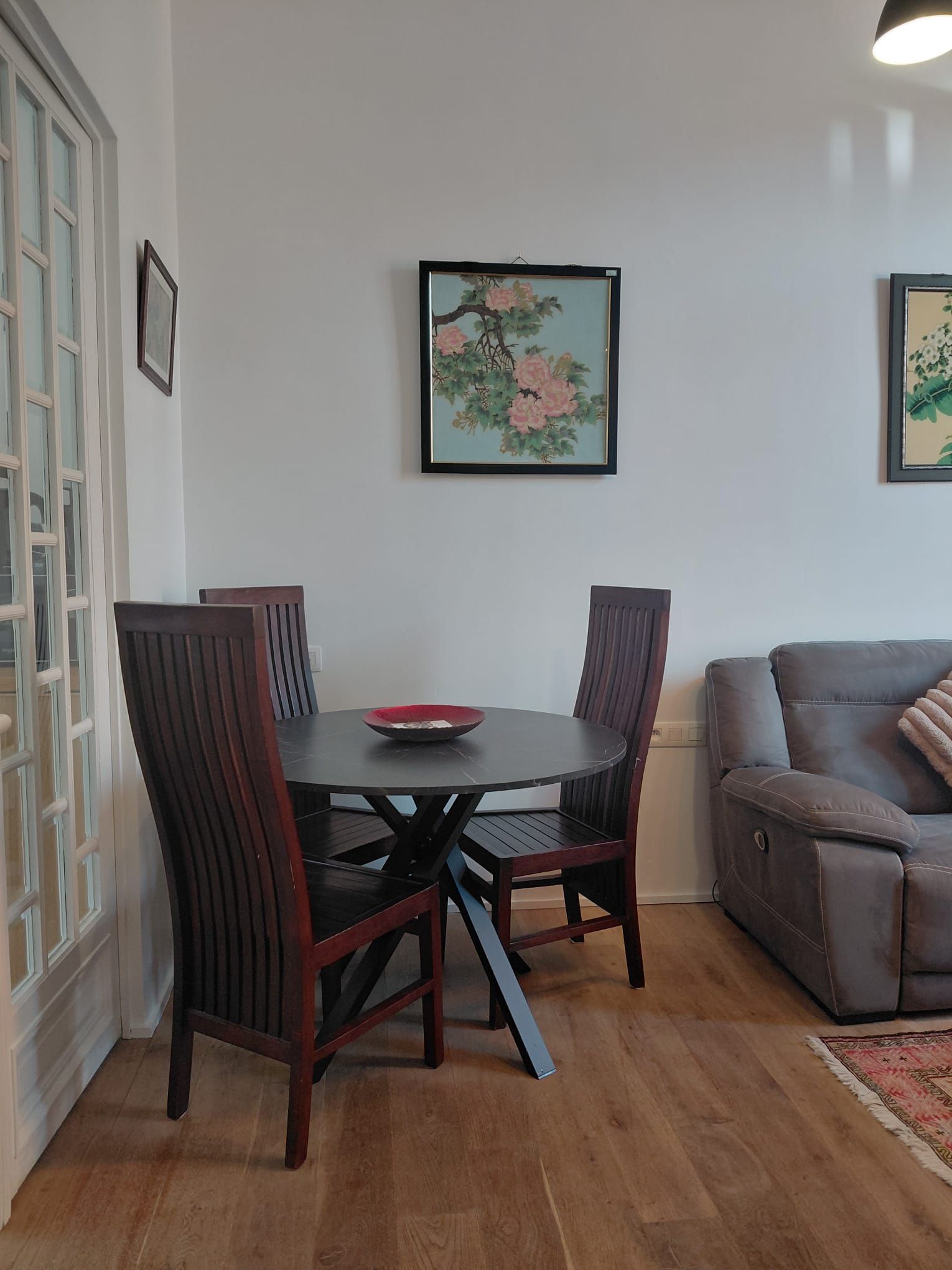 A dining area with a round table, four chairs, and two framed artworks on the wall.