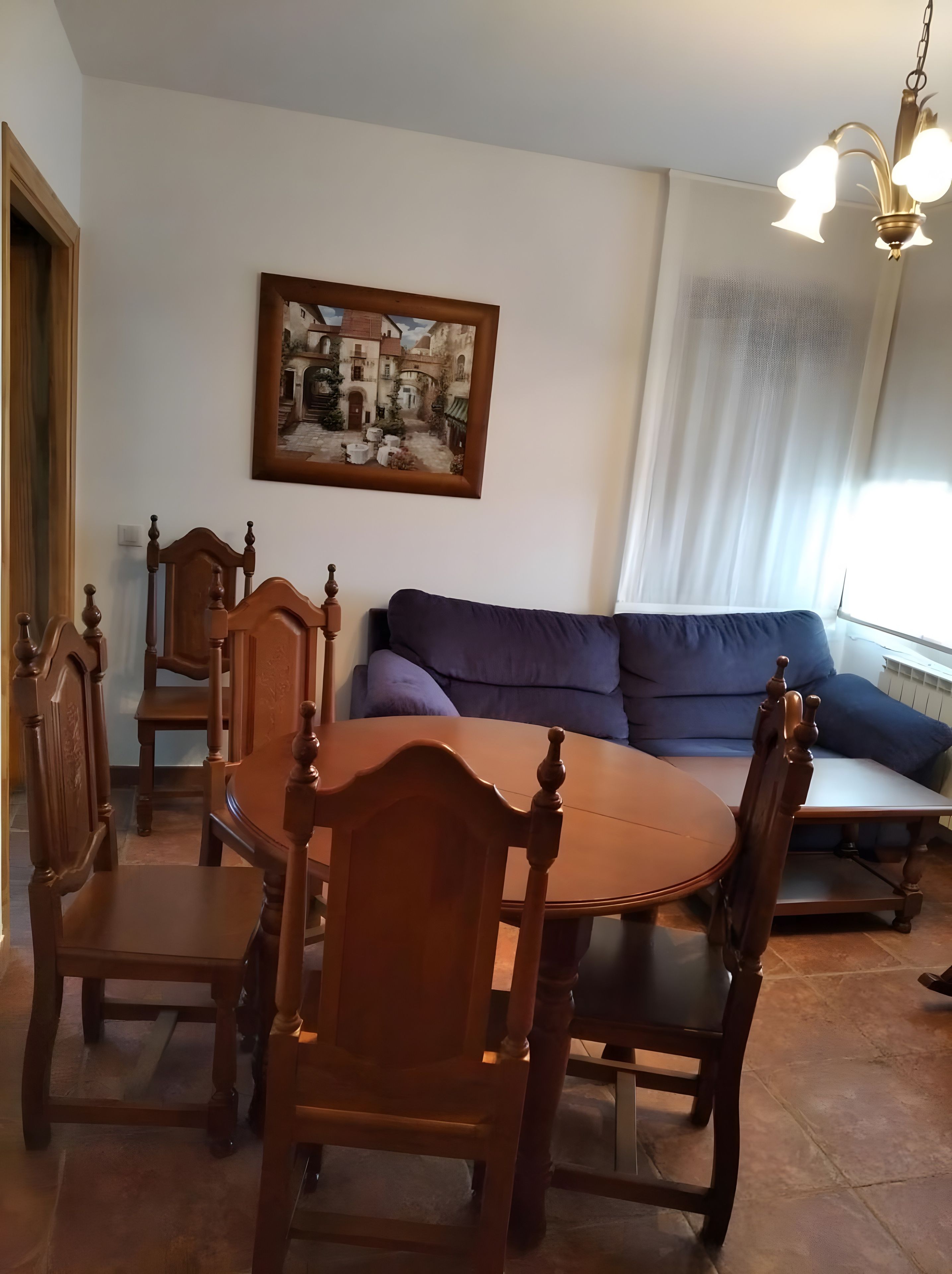 A dining area with a round table and wooden chairs, a sofa, and a painting on the wall.