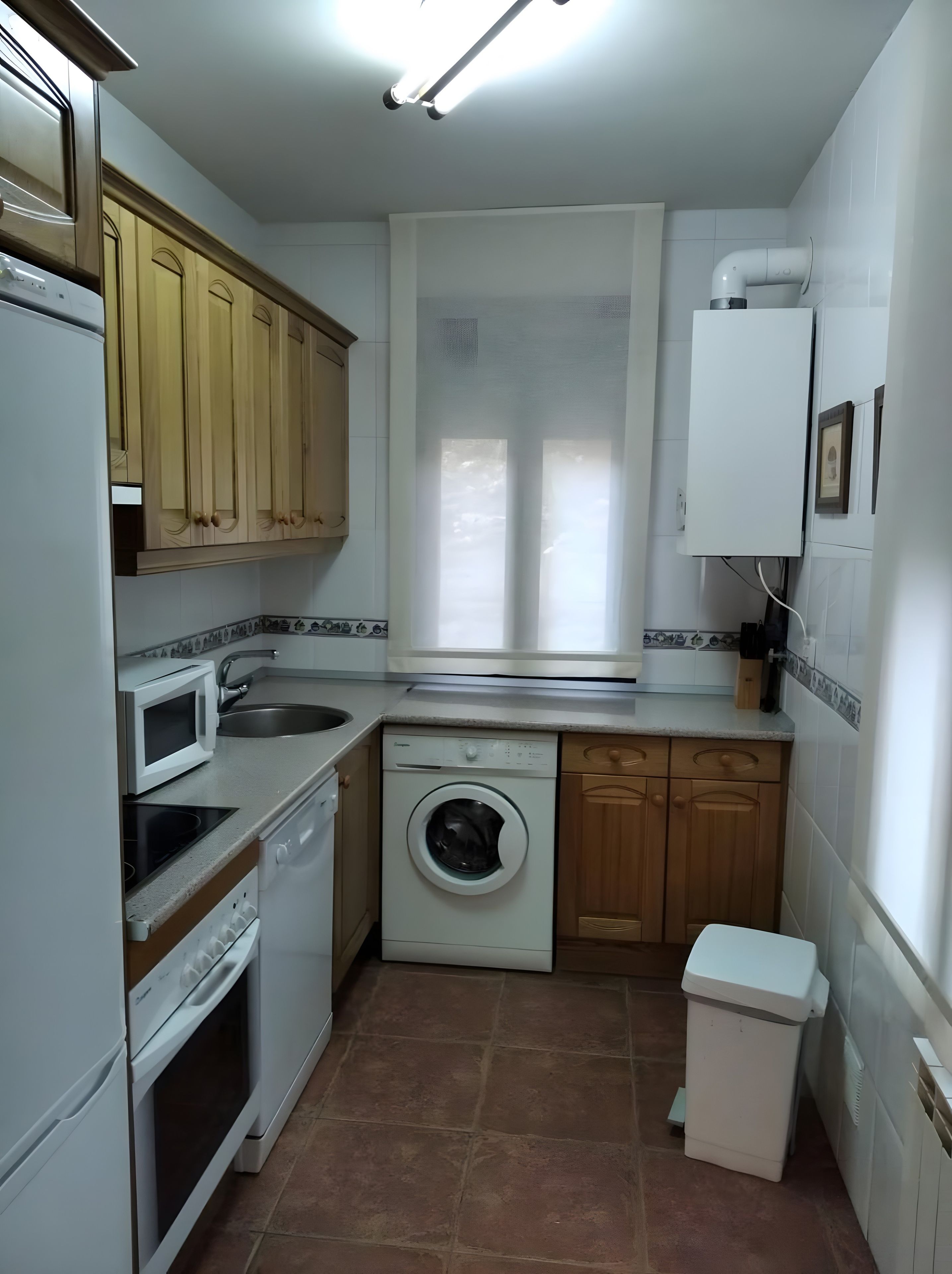 Una cocina compacta con lavadora, microondas y armarios de madera.