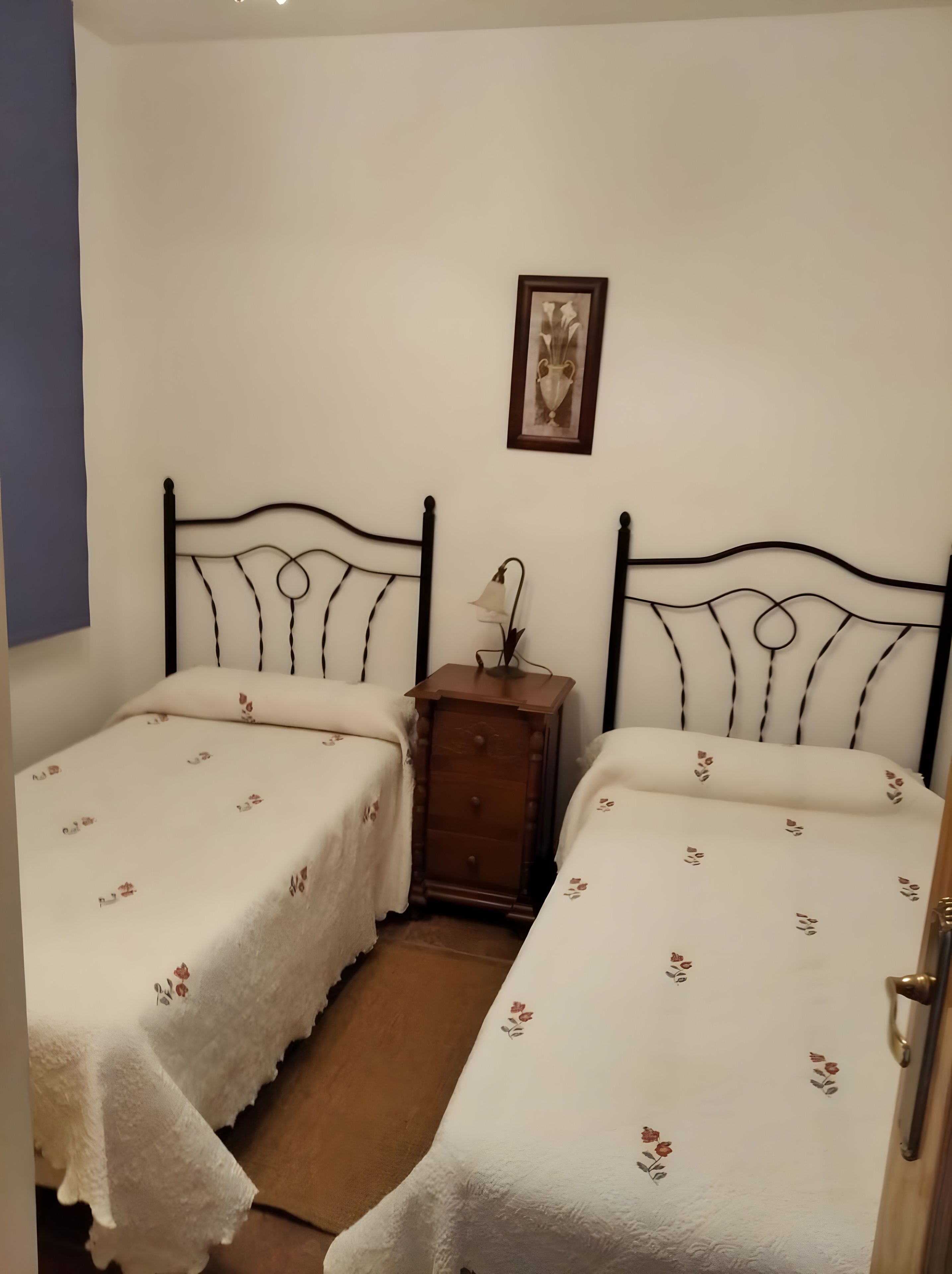 A room with two beds, a nightstand, and a framed picture on the wall.
