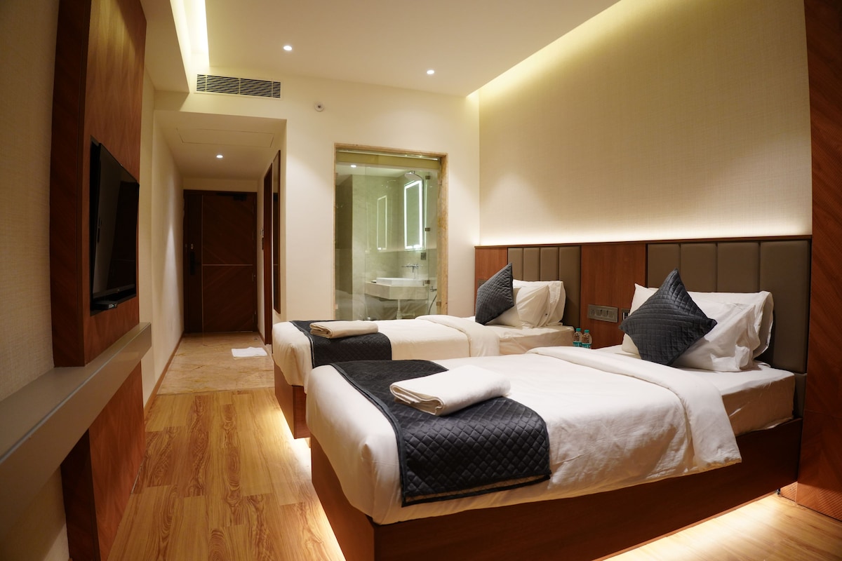 A hotel room with two beds, a television, and a bathroom visible through a glass door.