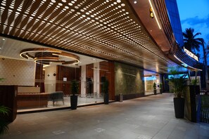 A hotel entrance with a modern design, featuring a patterned ceiling, a reception area with a seating area, and a large potted plant. - Crescent Hotel (Mysuru)