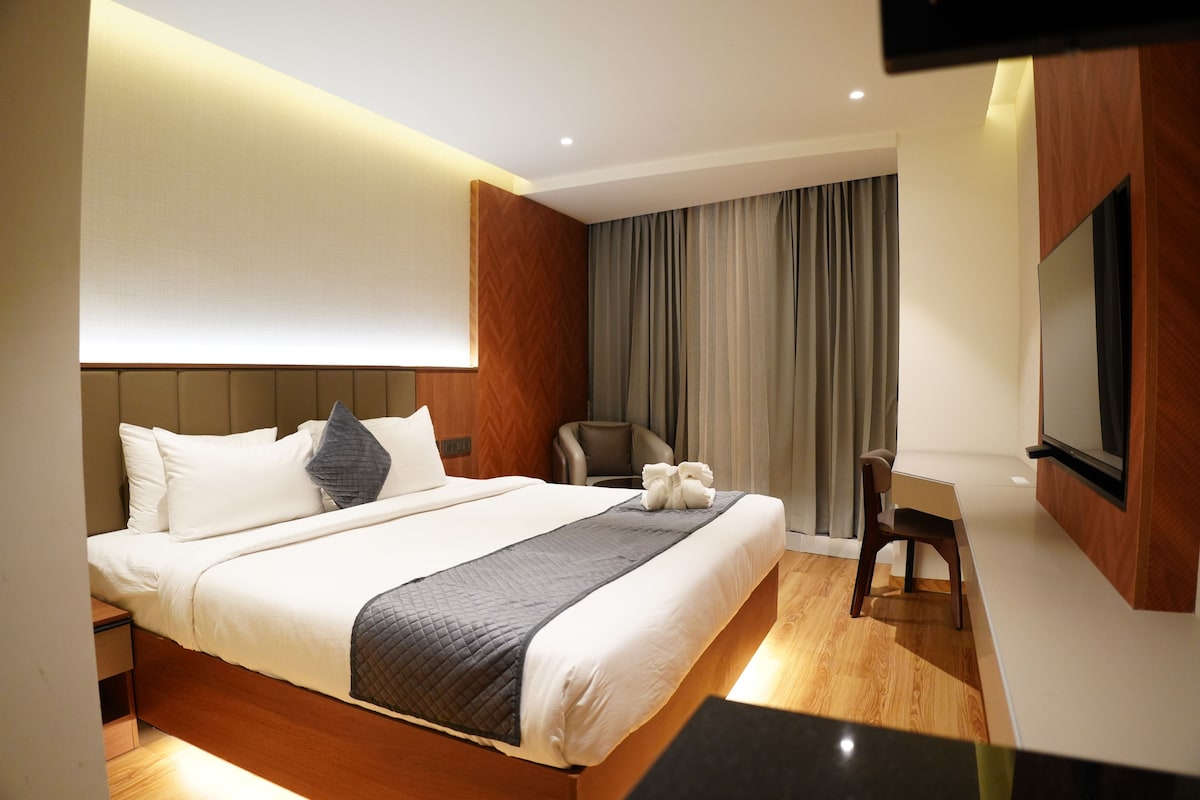 A hotel room with a bed, a desk, a chair, a TV, and a curtain.