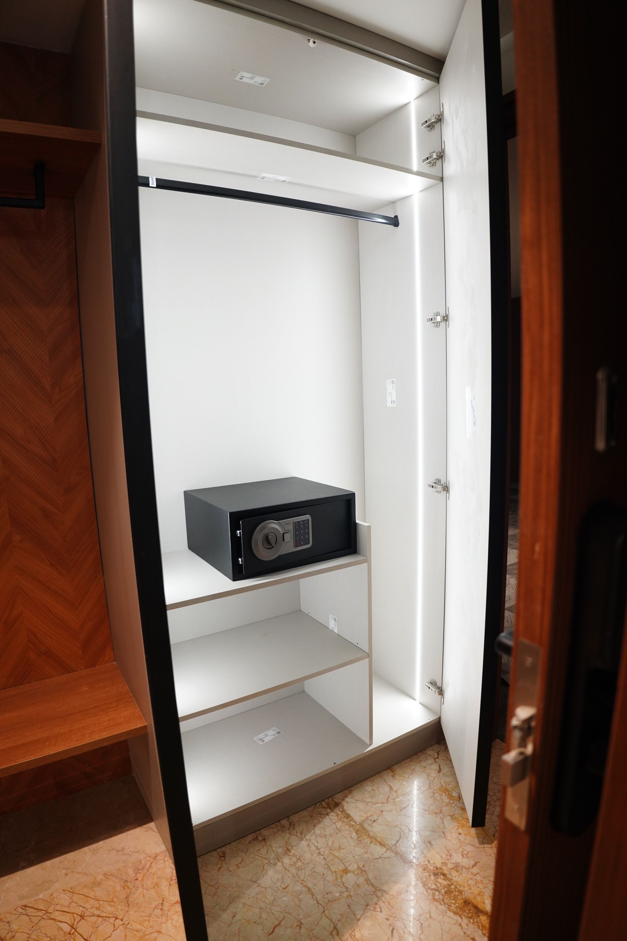 A walk-in closet with a black safe on the bottom shelf, a wooden floor, and a white door.