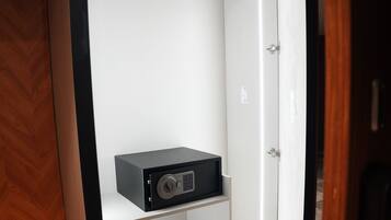A walk-in closet with a black safe on the bottom shelf, a wooden floor, and a white door.