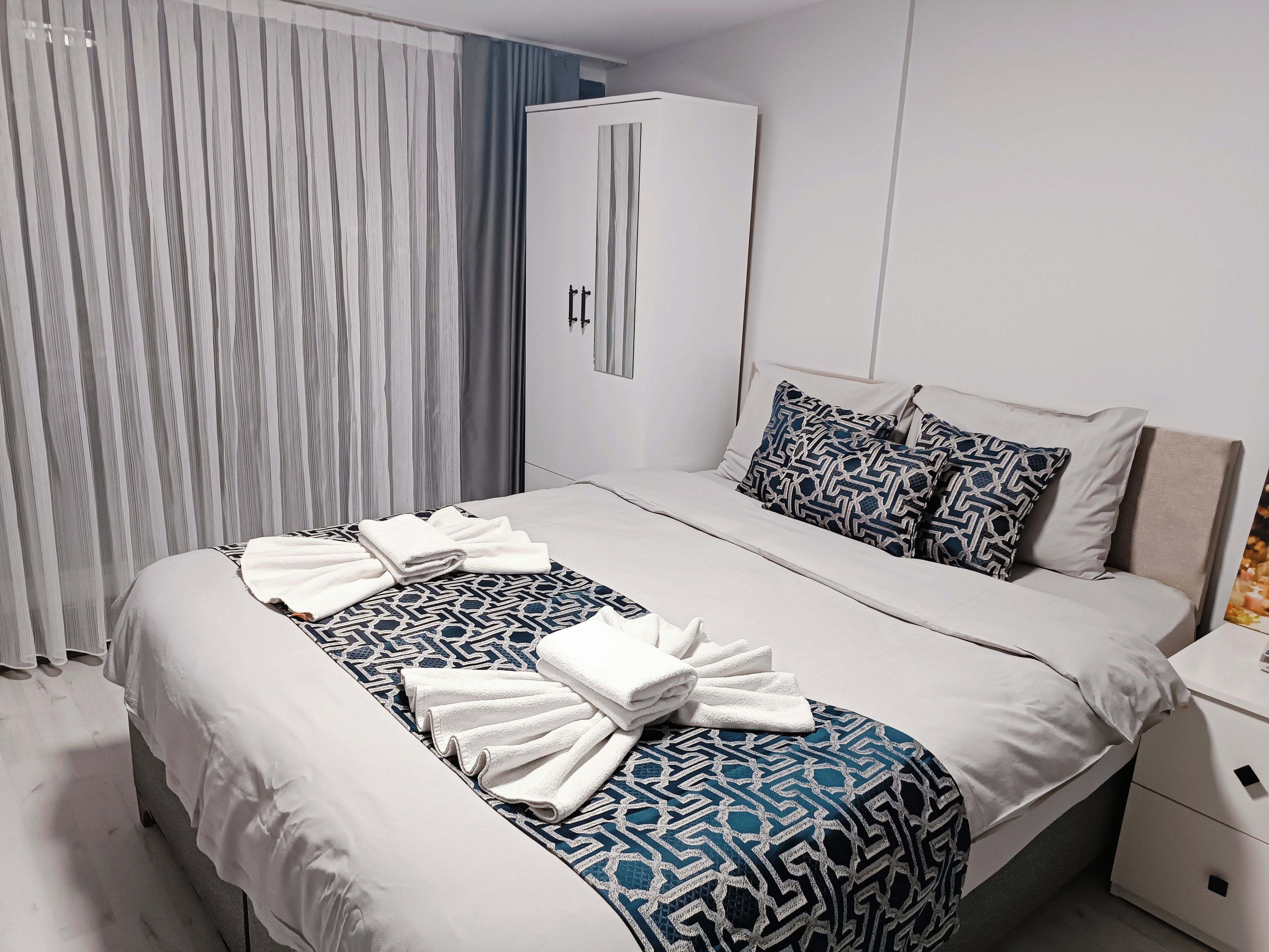 A hotel room with a bed, a wardrobe, a nightstand, and a curtain.