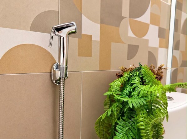 A bathroom with a shower head mounted on a tiled wall, a potted fern plant, and a toilet visible in the background. - New Listing (Americana)