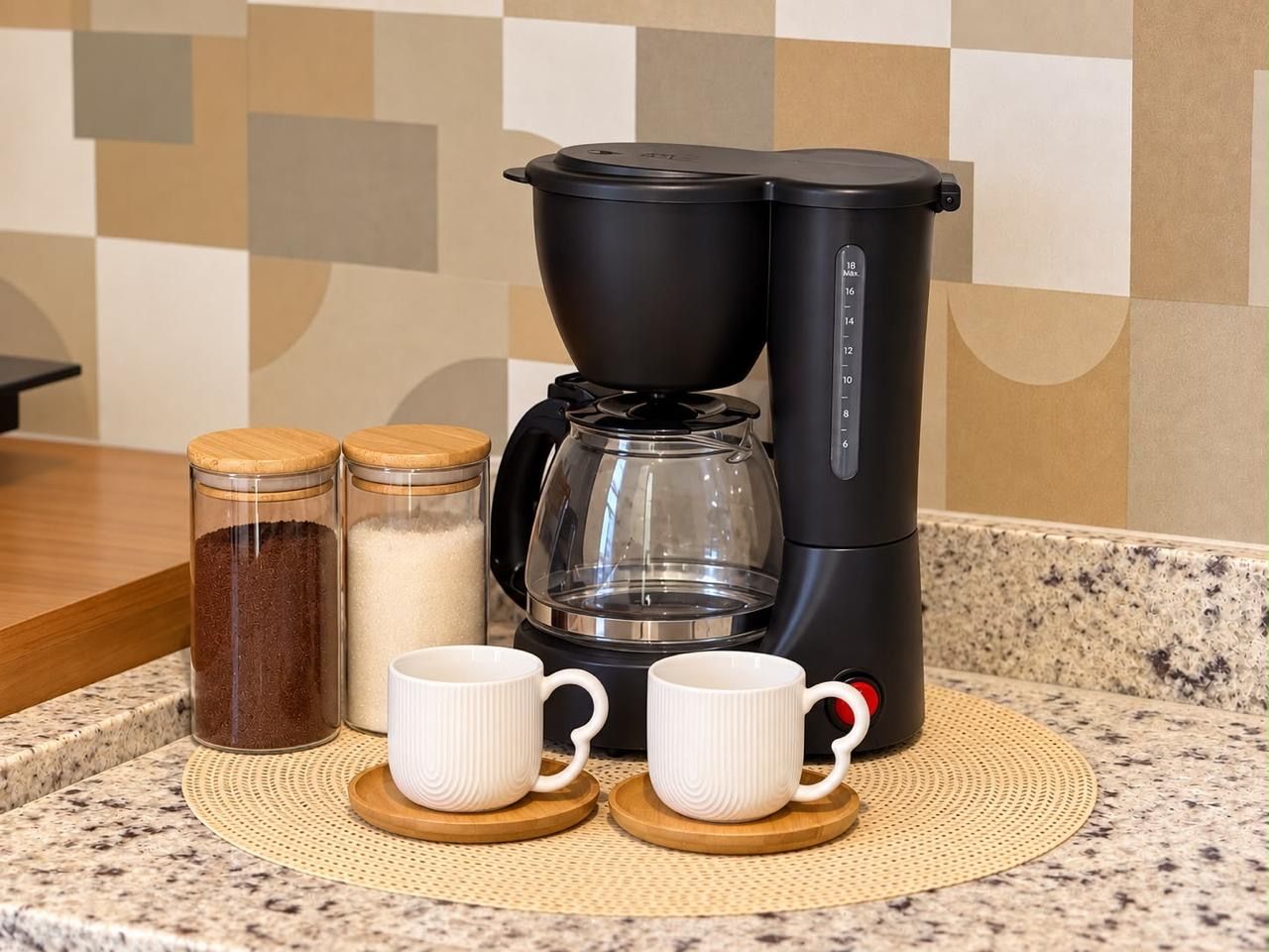 A coffee maker, two cups, and two containers on a kitchen counter.